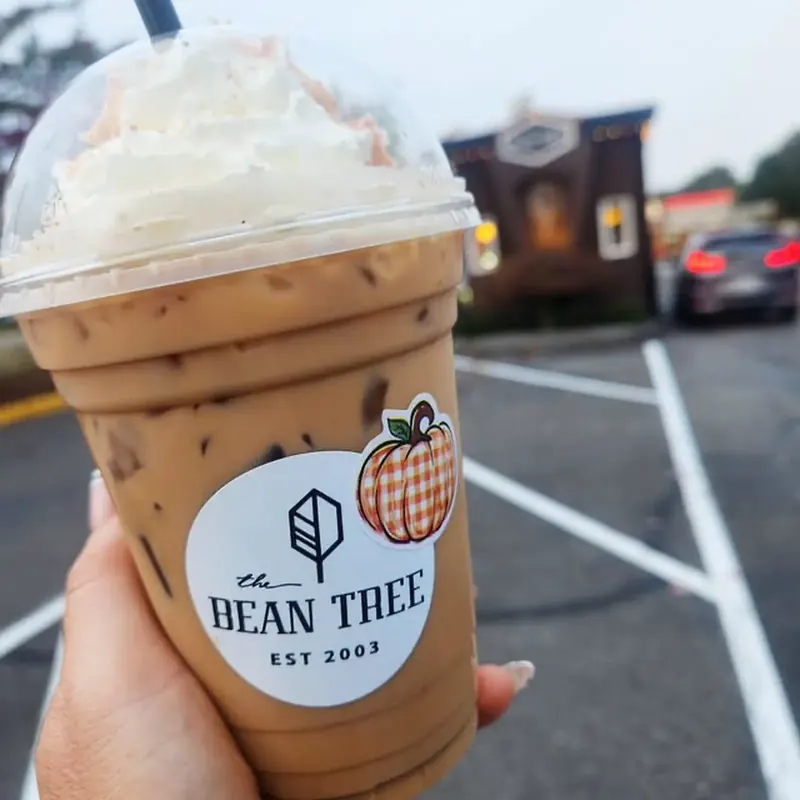 Hand holding a Bean Tree iced latte with whipped cream in front of the espresso stand at dusk