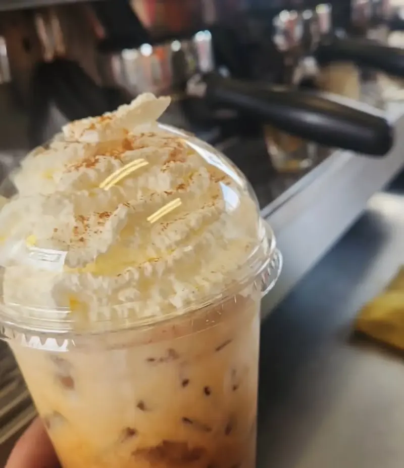 Iced latte with cinnamon-dusted whipped cream in front of the espresso machine
