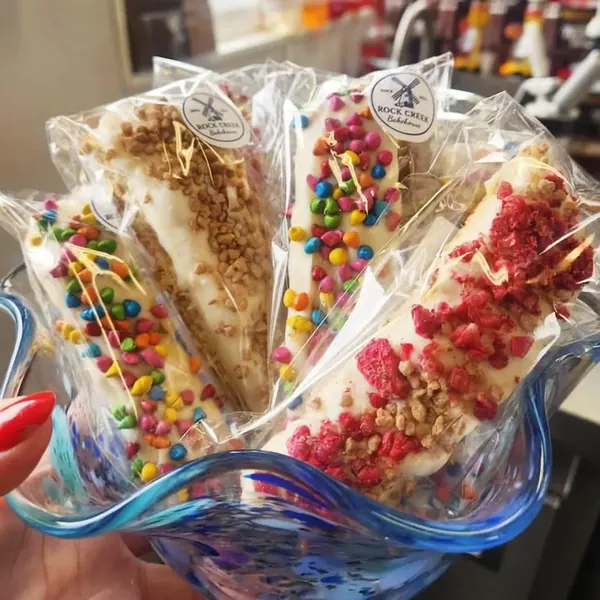 Wrapped white-chocolate-dipped treats with rainbow, toffee and berry toppings in a blue glass bowl